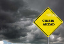 A yellow warning sign that reads 'CRISIS AHEAD' against a backdrop of dark, stormy clouds