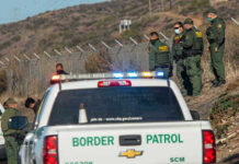 Border Patrol agents and vehicles at fenced border area.