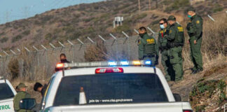 Border Patrol agents and vehicles at fenced border area.