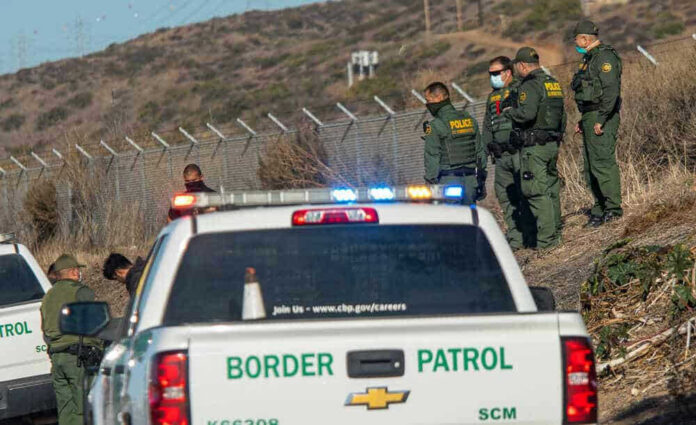 Border Patrol agents and vehicles at fenced border area.