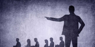AI Becomes Layoff King In April Shadows of laid-off workers walking, large figure pointing.