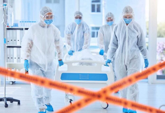 Healthcare workers in protective gear transporting a patient in a hospital