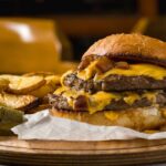 A double cheeseburger with melted cheese and pickles served with potato wedges