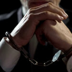 Handcuffed person in suit, hands clasped together.
