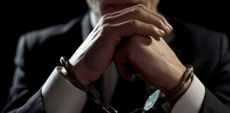 Handcuffed person in suit, hands clasped together.