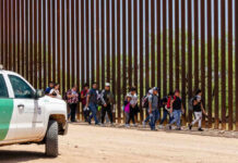 Border Blitz: $70B Power Play Group of people walking by a border fence.