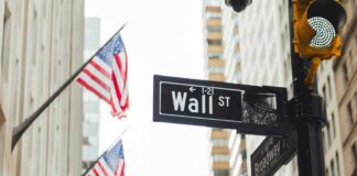 Wall Street sign and traffic light in a city street with American flags