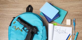A blue backpack with a handgun and school supplies on a wooden surface