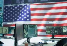 A command center with multiple computer monitors and an American flag in the background