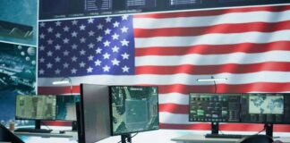 A command center with multiple computer monitors and an American flag in the background