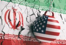 A wrecking ball painted with the American flag is breaking through a wall featuring the Iranian flag