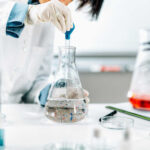 Scientist in a lab using a pipette to transfer liquid into a flask