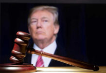 Judge Slaps Down Trump Branding Move Gavel in foreground with blurry man in background.