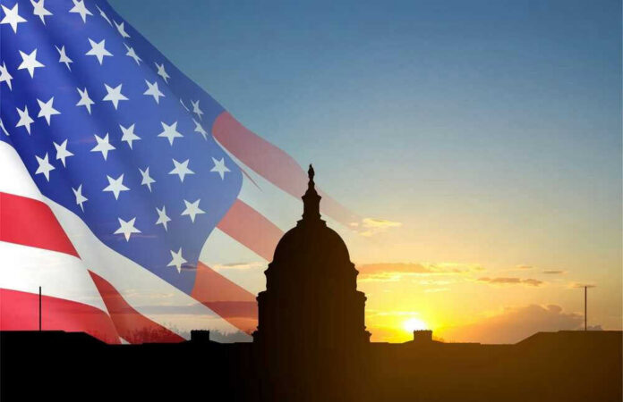 shutterstock_2367993607 Capitol building silhouette with American flag at sunrise.