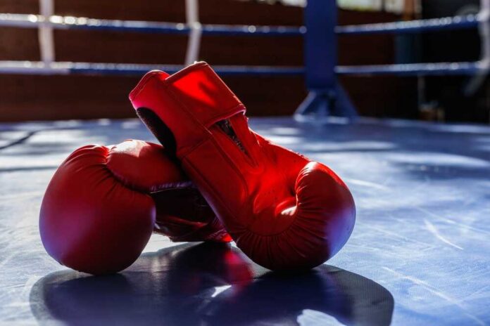 Bright,Red,Boxing,Gloves,On,A,Gym,Ring,Mat,With An empty boxing ring illuminated by bright lights in a sports arena