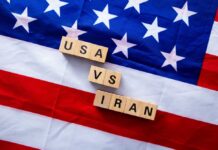 Iran Hits U.S. Base; American Troops Killed A wrecking ball painted with the American flag is breaking through a wall featuring the Iranian flag