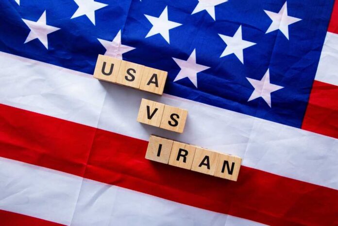 A wrecking ball painted with the American flag is breaking through a wall featuring the Iranian flag