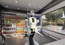 A humanoid robot using a tablet in an industrial setting with robotic arms in action