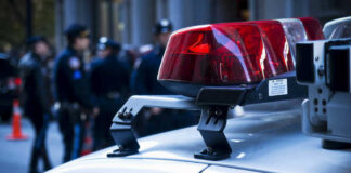 Shots Ring Out In Grocery Store – 2 Down Police car lights with officers blurred in background.