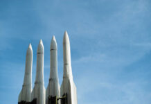Four white missile launchers pointing upward against a blue sky