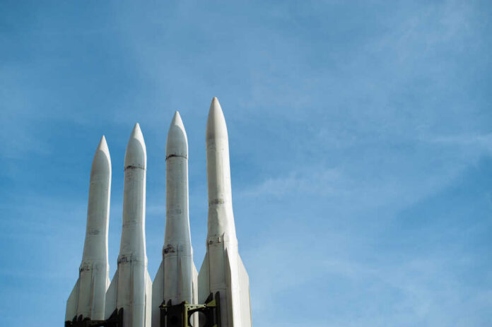 Four white missile launchers pointing upward against a blue sky
