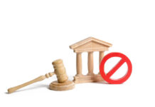 Wooden gavel, courthouse model, and red prohibition sign on white background