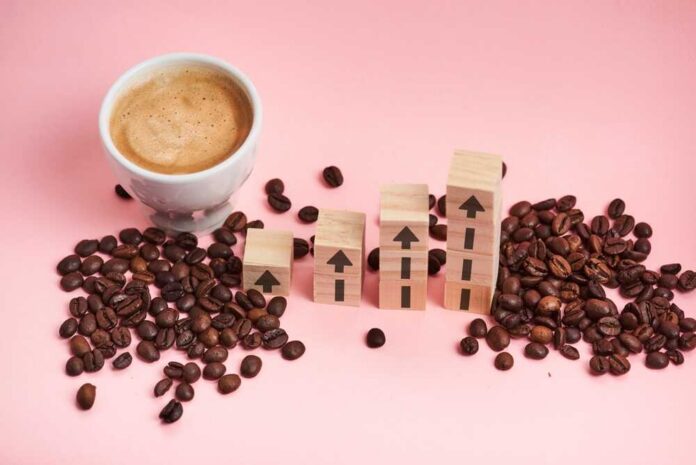 Coffee,Beans,And,Cup,With,Wooden,Blocks,Stacked,In,A A cup of coffee next to wooden blocks with upward arrows and scattered coffee beans on a pink background