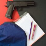 Handgun near notebook, pencils, and blue backpack