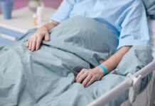 Hospital Mix-Up Leaves Grandma Paralyzed Patient resting in a hospital bed with hands on blanket