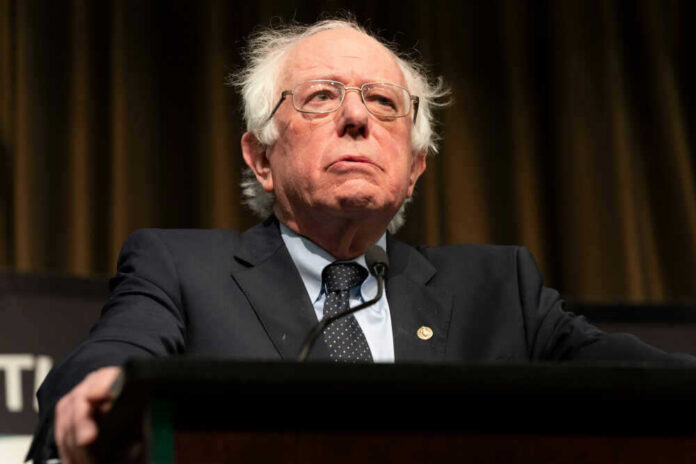 shutterstock_1360787486 Bernie Sanders in suit speaking at podium.