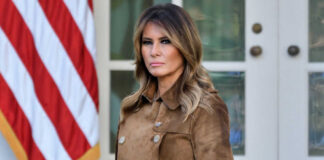 Melania Trump standing outdoors in a brown suede trench coat