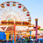 Colorful amusement park scene featuring a ferris wheel and roller coaster at sunset