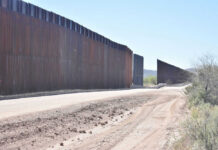 Dirt road beside tall metal border wall