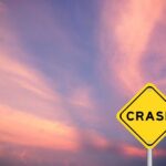Yellow crash warning sign against a pink and purple sunset sky