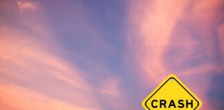 Yellow crash warning sign against a pink and purple sunset sky