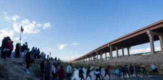 People crossing a shallow river near an overpass