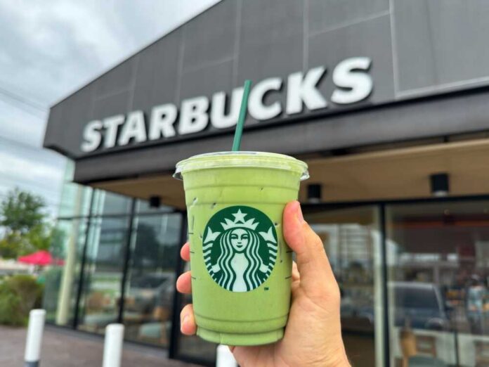 Hand holding a green matcha drink in front of a Starbucks store