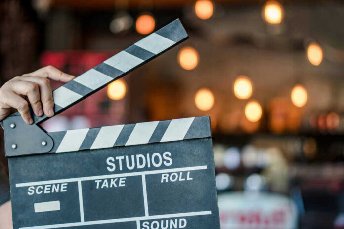 shutterstock_781592248 Hand holding a movie clapperboard in studio setting.