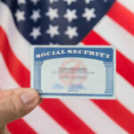 Surprise COLA Jolt Hits 2027 Hand holding social security card, American flag background.