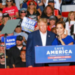 Brutal Crash Hammers Trump Donald Trump at a rally with a woman speaking at the podium; Alexandros Papadiamantis, Margarita Stolbizer, and David Lowy are present in the crowd