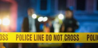Police tape at a night scene with blurred officers in the background
