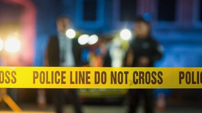 Police tape at a night scene with blurred officers in the background