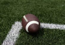 A brown football resting on green artificial turf near a white line