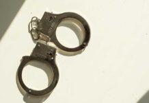 53 Bodies – One Criminal A pair of metallic handcuffs resting on a light surface