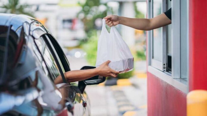 Young,Man,Receiving,Coffee,At,Drive,Thru,Counter.,,Drive,Thru Customer receives a takeout bag at a drive-thru window