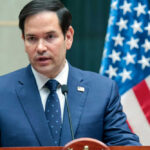 Marco Rubio speaking at a podium with a U.S. flag in the background