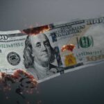 Burning US hundred-dollar bill with embers and holes
