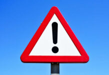 A triangular warning sign with an exclamation mark against a blue sky