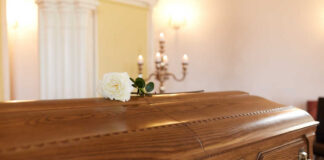 A wooden casket with a white rose placed on top in a solemn setting