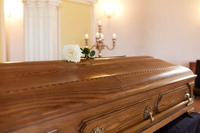 Funeral,And,Mourning,Concept,-,White,Rose,Flower,On,Wooden A wooden casket with a white rose placed on top in a solemn setting